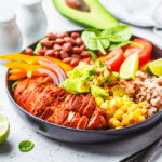 Mexican chicken burrito bowl with rice, beans, tomato, avocado,corn and spinach, white background. Mexican cuisine food concept.