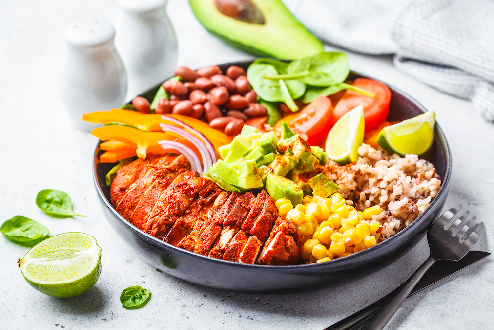 Mexican chicken burrito bowl with rice, beans, tomato, avocado,corn and spinach, white background. Mexican cuisine food concept.