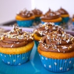 Vanilla Cupcakes with Chocolate Buttercream Frosting on a blue plate with a more cupcakes on a tray in the background