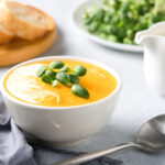Butternut squash cream soup garnished with heavy cream and fresh sunflower microgreen. Creamy pumpkin fall soup in white bowl on the gray table. Selective focus
