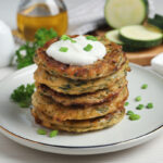 Delicious zucchini pancakes with sour cream served on white wooden table