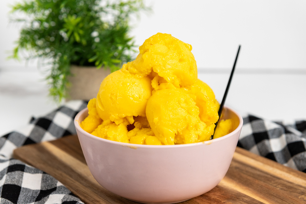 Homemade Mango Sorbet on a wooden board with a plant in the background sitting on black and white check fabric