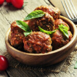 Meatballs of pork and beef with spicy tomato sauce in bowl, vintage wooden background, selective focus