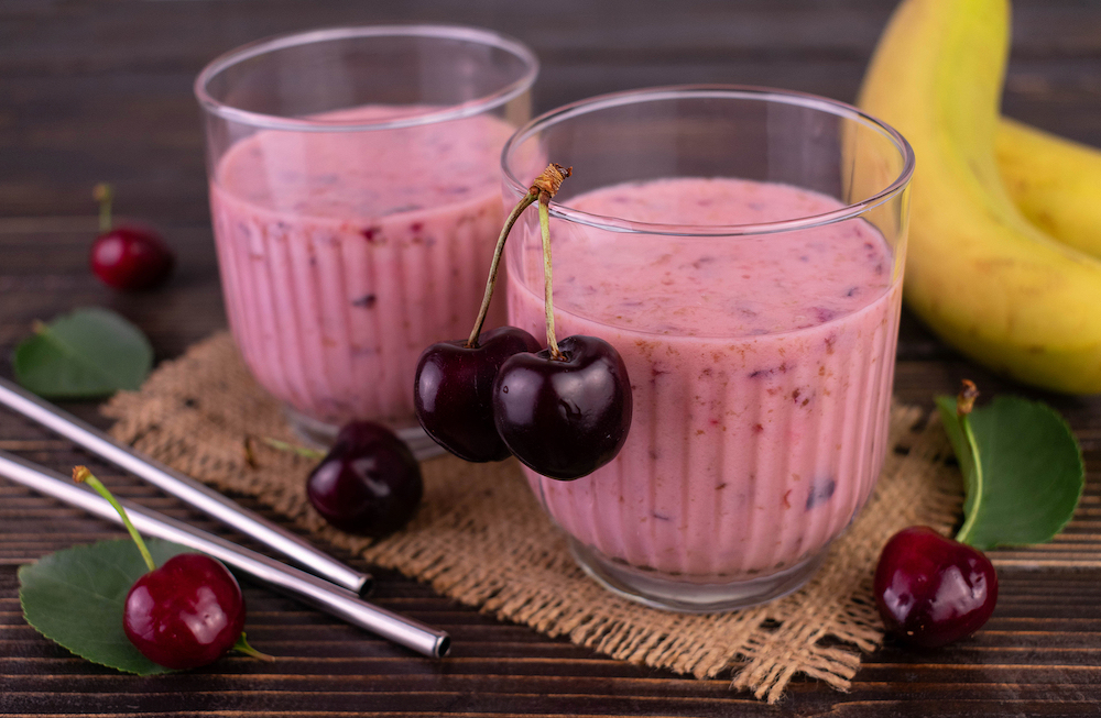 Two glasses of cherry and banana smoothie on a dark wooden background.