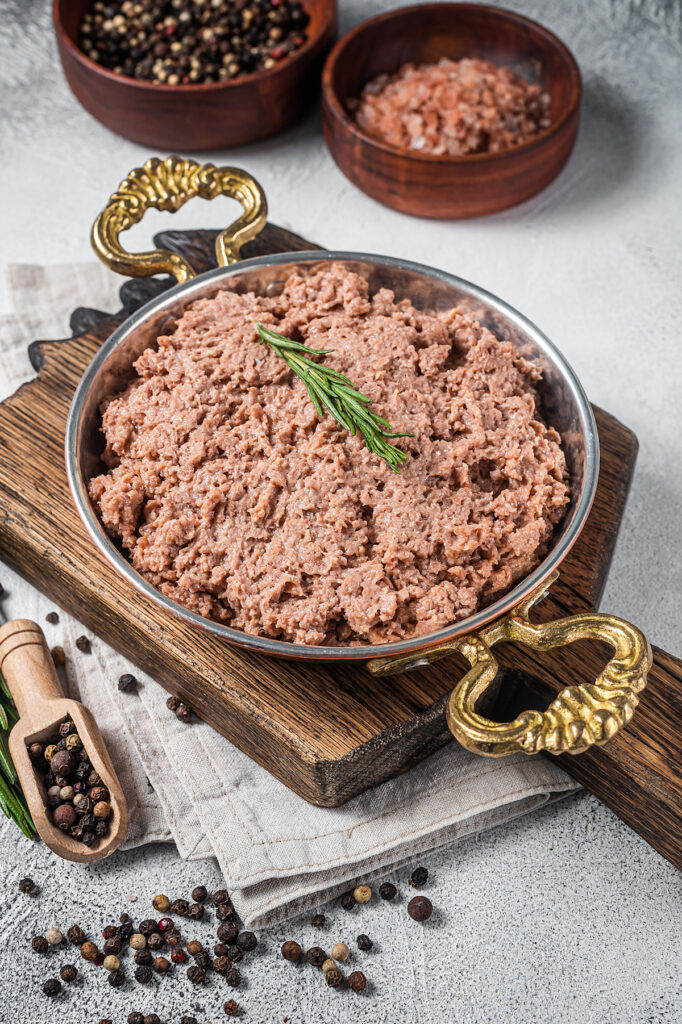 Uncooked vegan mince meat, raw plant based meat with thyme in skillet. White background. Top view