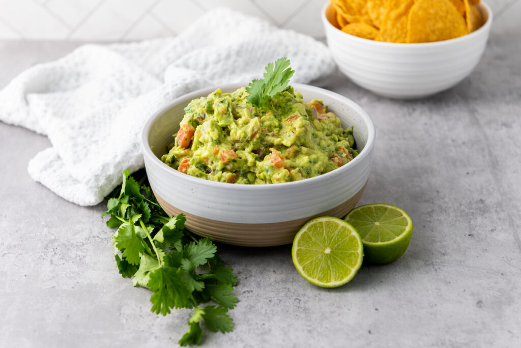 Homemade Guacamole in a white bowl with corn chips in the background
