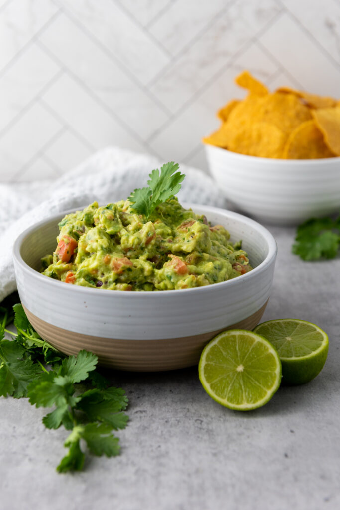 Homemade Guacamole in a white bowl with corn chips in the background