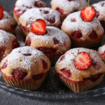 Homemade strawberry muffins sprinkled with powdered sugar on gray background. Close-up