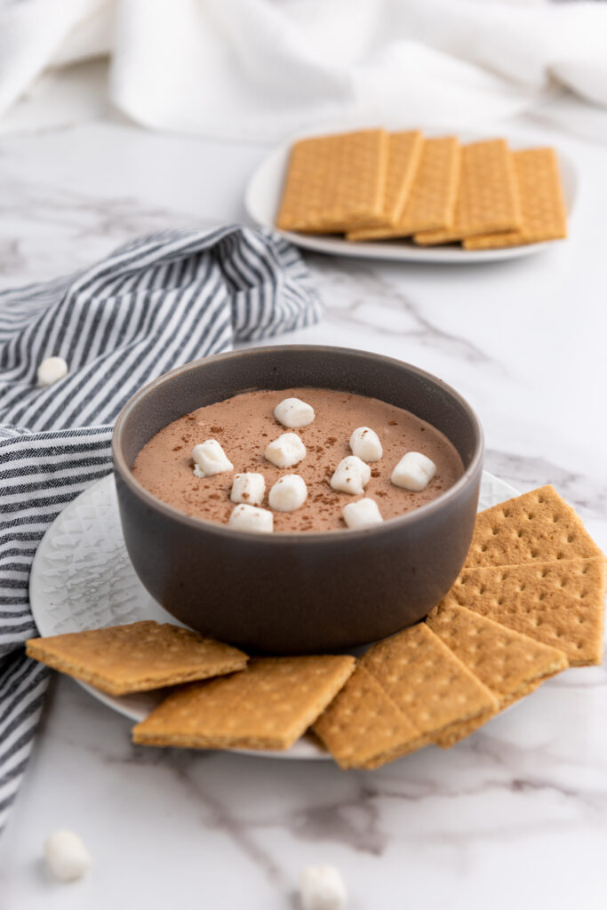 Hot Cocoa Dip topped with mini marshmallows in a plate bowl with graham crackers on the side.