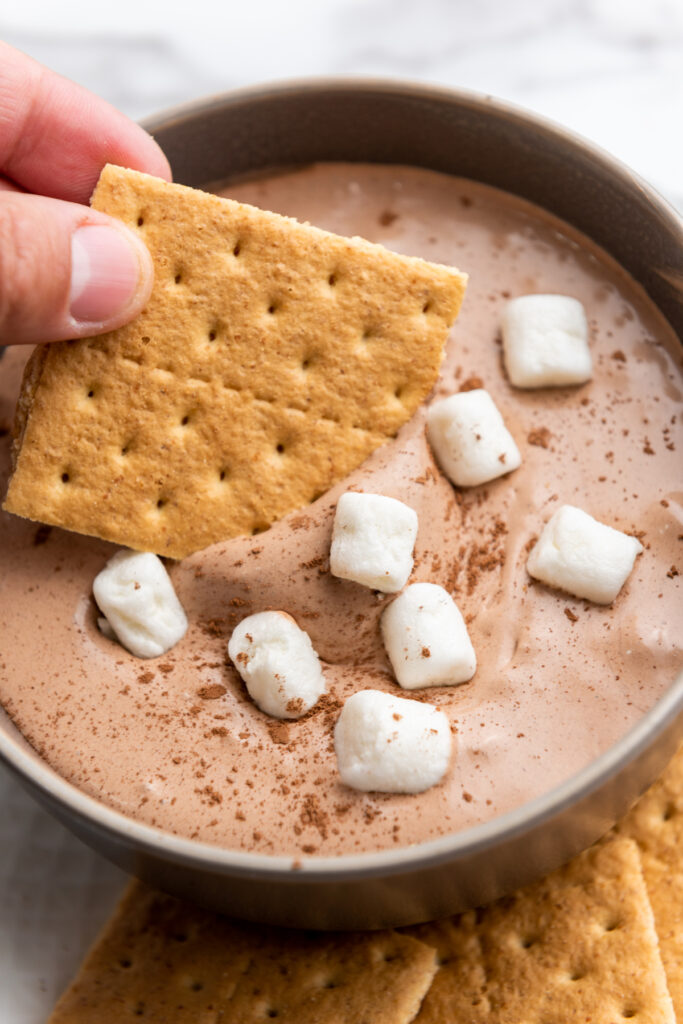 Hot Cocoa Dip topped with mini marshmallows in a plate bowl with graham crackers on the side.