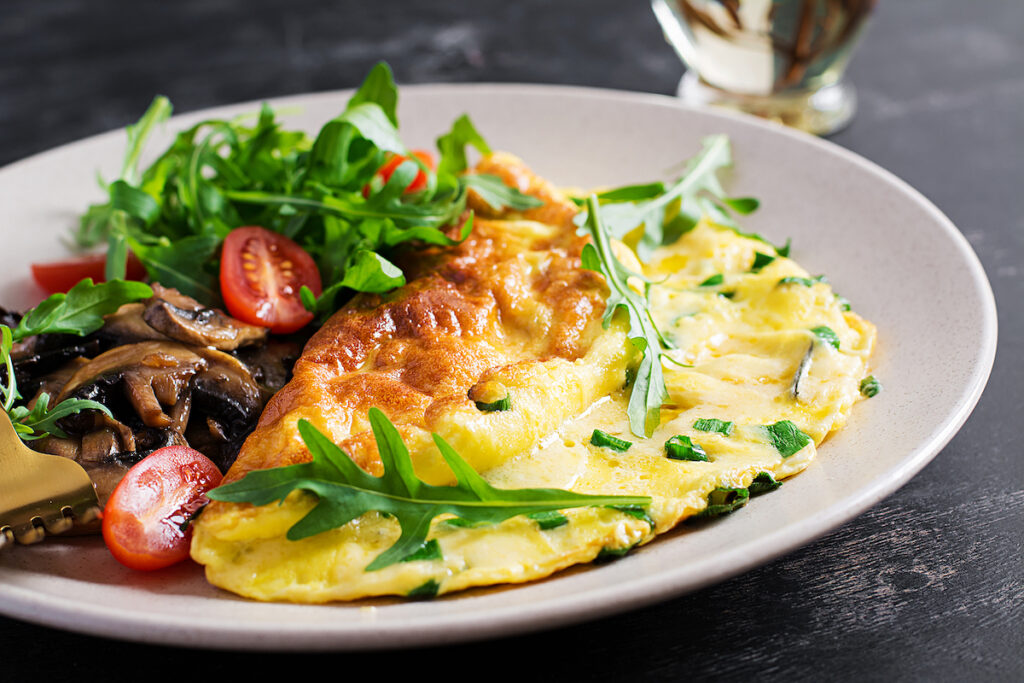 Omelette with cheese, green herbs and fried mushrooms on plate.  Frittata - italian omelet