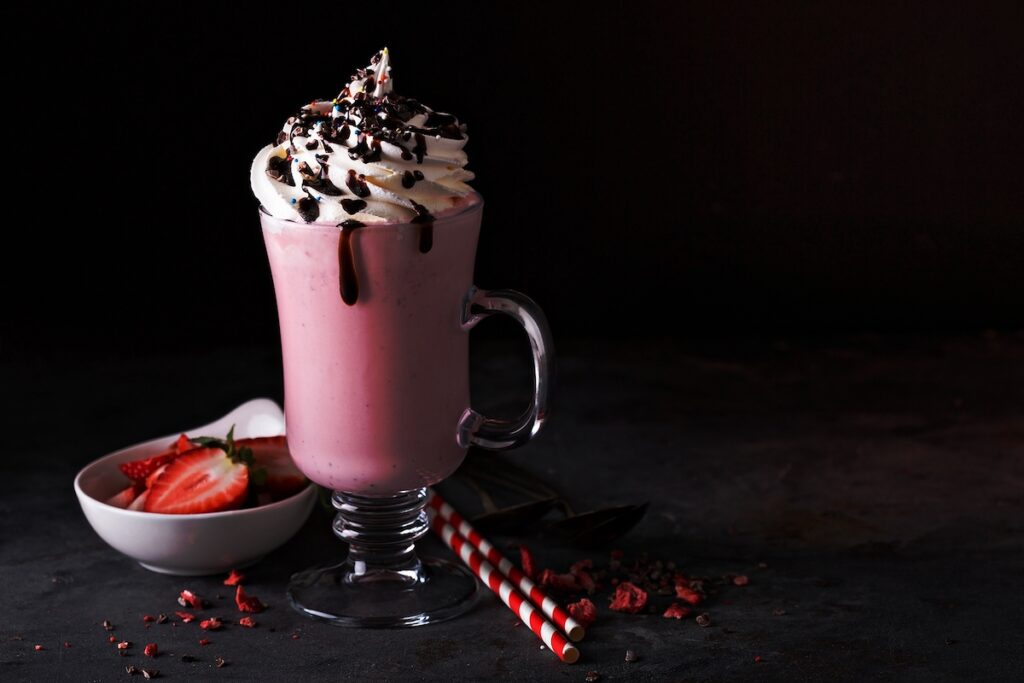 Strawberry milkshake with whipped cream and chocolate syrup with copyspace on dark background