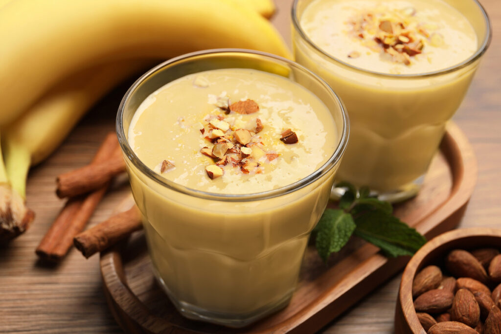 Tasty banana smoothie with almond and cinnamon on wooden table, closeup