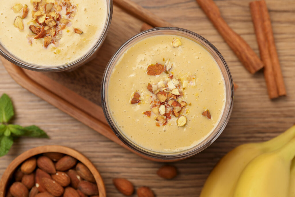 Tasty banana smoothie with almond and cinnamon on wooden table, flat lay