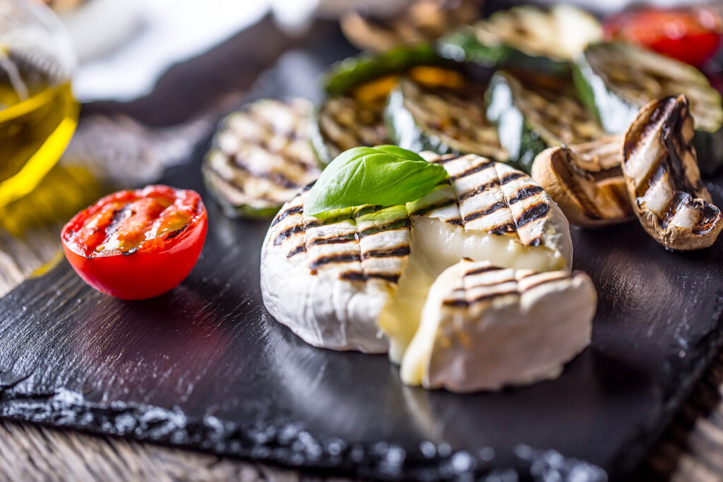 Camembert cheese. Grilled camembert cheese with zucchini tomatoes olive oil and basil leaves.