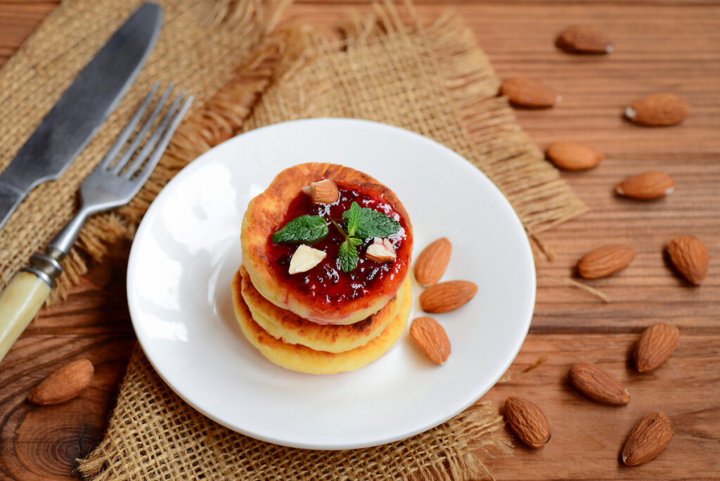 Fried cottage cheese pancakes with berry jam, almonds nuts and mint on a served plate. Delicious cottage cheese almond flour pancakes